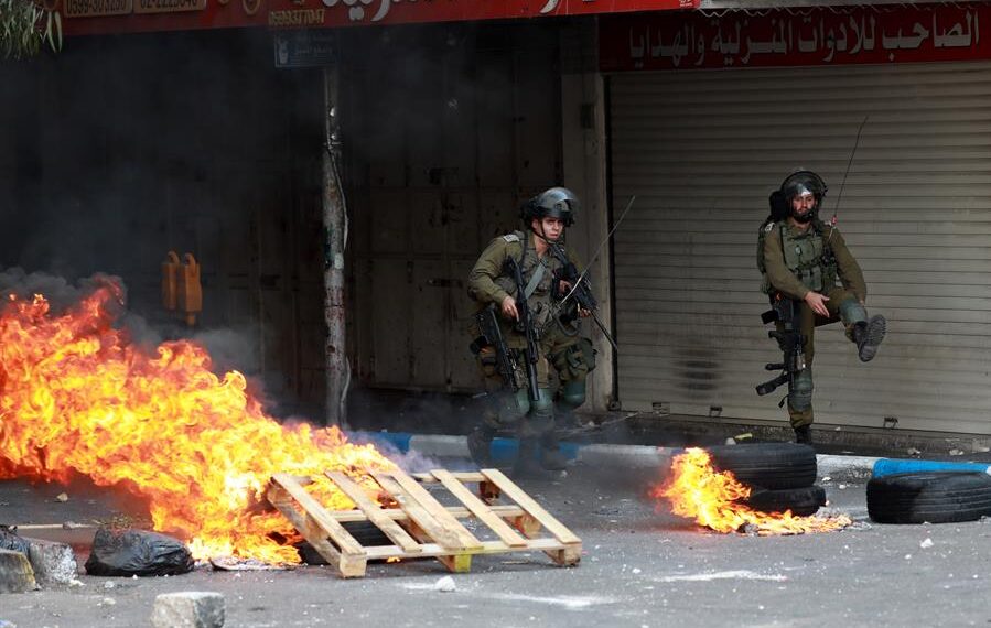 Soldados israelíes toman posiciones cerca de barricadas en llamas durante enfrentamientos con manifestantes palestinos en la ciudad cisjordana de Hebrón, el 20 de octubre de 2022. EFE/EPA/ABED AL HASHLAMOUN