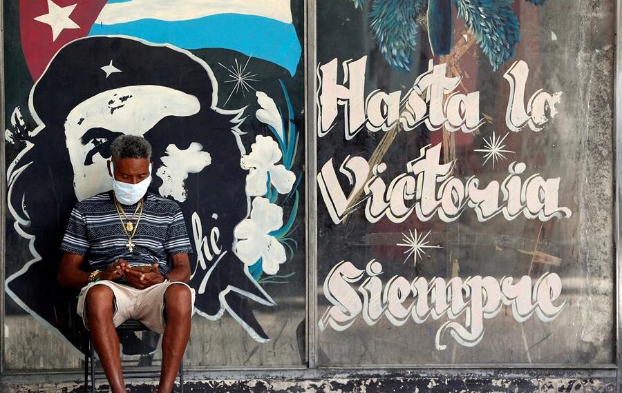 Un hombre con tapabocas revisa en su celular, junto a un graffitis con la imagen del guerrillero argentino-cubano Ernesto “Che” Guevara en La Habana (Cuba). Imagen de archivo. EFE/Ernesto Mastrascusa