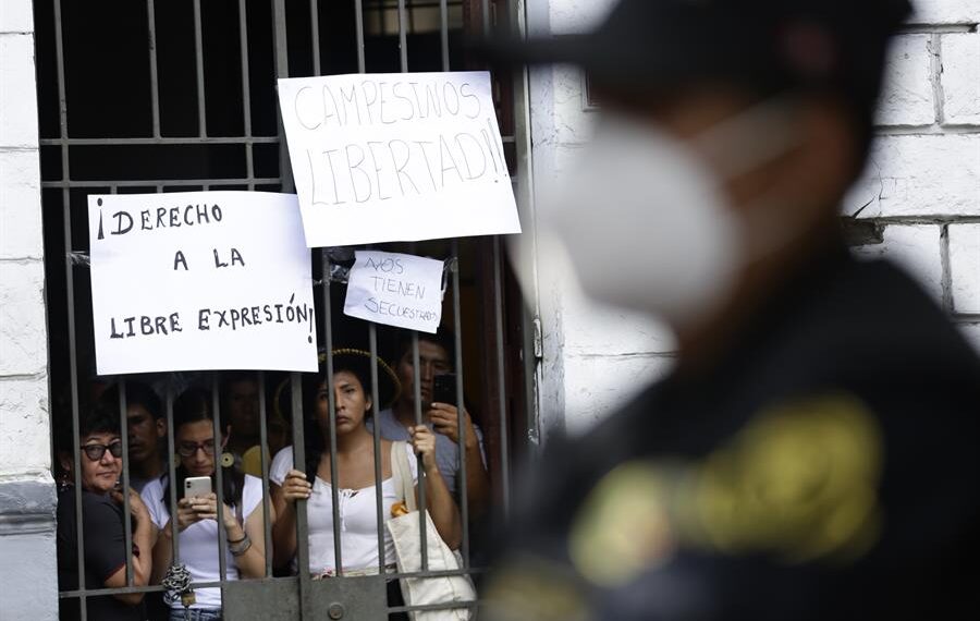 Varias personas observan desde una reja de la que cuelgan carteles de protesta durante la intervención policial a la Confederación Campesina del Perú (CCP), hoy, en Lima (Perú). EFE/Bienvenido Velasco