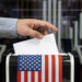 Election in USA. Man putting his vote into ballot box and American flag on background, closeup
