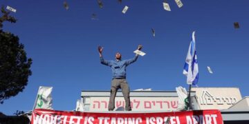 Un manifestante lanza dólares al aire durante una protesta contra la reforma del sistema judicial frente a la sede de la organización Americano-judía Kohelet Policy Forum, en Jerusalén (Foto: EFE)