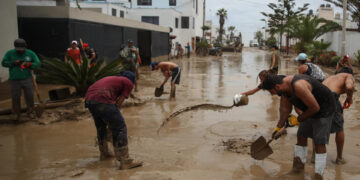 Fotografía de archivo, tomada el pasado 15 de marzo, en la que se registró a un grupo de personas al remover el lodo de una calle anegada por las lluvias, en el balneario de Punta Hermosa, al sur de Lima (Perú). EFE/Paolo Aguilar