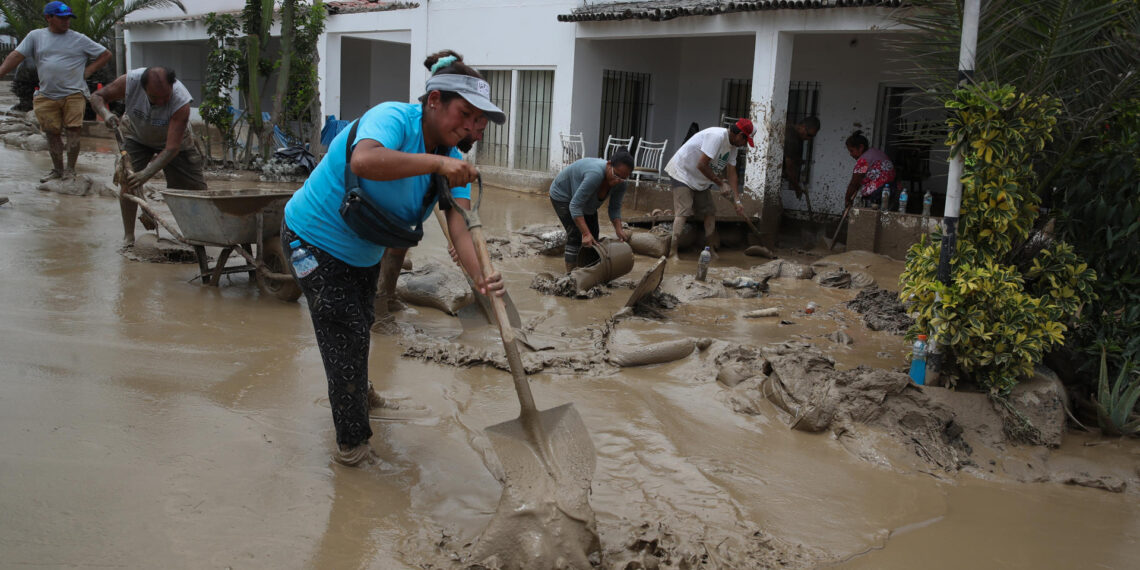 Personas ayudan a remover el lodo en una calle afectada por las lluvias, en el balneario de Punta Hermosa al sur de Lima (Perú), en una fotografía de archivo. EFE/Paolo Aguilar