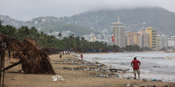 Personas caminan por una playa llena de basura debido a las fuertes lluvias hoy, en el balneario de Acapulco, estado de Guerrero (México). EFE/David Guzmán