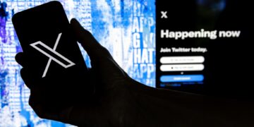 Fotografía que muestra un usuario mientras sostiene un teléfono móvil que muestra el logotipo 'X' frente a la página principal de Twitter. EFE/EPA/Etienne Laurent