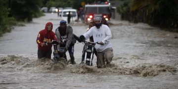 Personas cruzan con dificultad la carretera que se encuentra inundada producto de las intensas lluvias, hoy en San José de Ocoa (República Dominicana). EFE/Orlando Barría