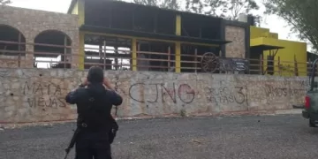 Un policía toma una foto de una barda rayada con las siglas del CJNG. Foto: Especial