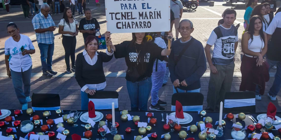 Una mujer sostiene un cartel pidiendo la libertad para el militar venezolano José Marín Chaparro en una manifestación frente a una mesa decorada con motivos navideños en Caracas (Venezuela). EFE/ Miguel Gutiérrez