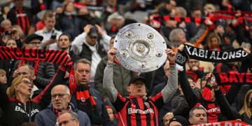 A Bayer Leverkusen fan holds up a mock-up of the Bundesliga trophy prior to the German first division Bundesliga football match Bayer 04 Leverkusen v TSG 1899 Hoffenheim in Leverkusen, western Germany on March 30, 2024. (Photo by INA FASSBENDER / AFP) / DFL REGULATIONS PROHIBIT ANY USE OF PHOTOGRAPHS AS IMAGE SEQUENCES AND/OR QUASI-VIDEO (Photo by INA FASSBENDER/AFP via Getty Images)